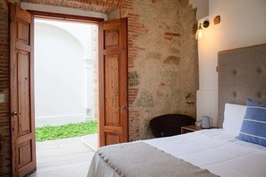A bedroom with a bed, a nightstand, a lamp, and a view of a courtyard. - Hotel Tabáa Oaxaca (Oaxaca)