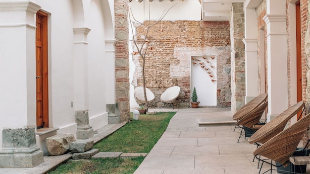 Un patio con muro de ladrillo, columnas blancas y sillas de mimbre.