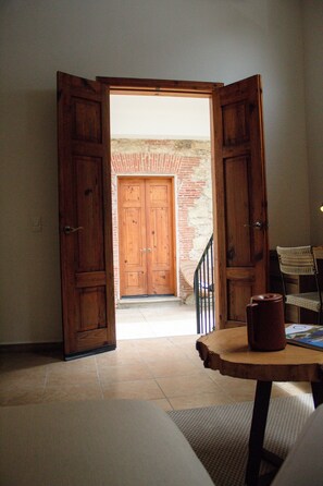 An open wooden door leading to a room with a brick wall, a wooden table, and a chair.