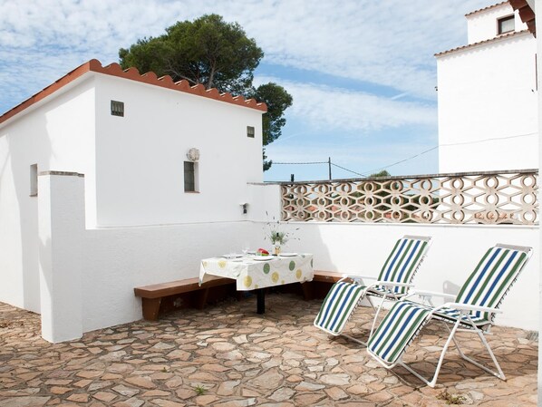 Un patio con una mesa preparada para dos, dos sillones reclinables a rayas y un piso de baldosas de piedra.