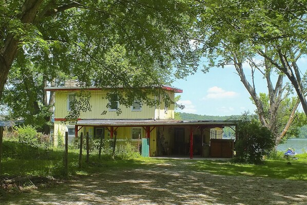 Una casa de dos pisos con porche, rodeada de árboles y vista al lago.