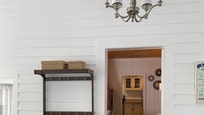 Une pièce avec un mur blanc, un plancher en bois, une étagère en bois foncé, un lustre et une porte donnant sur une autre pièce.