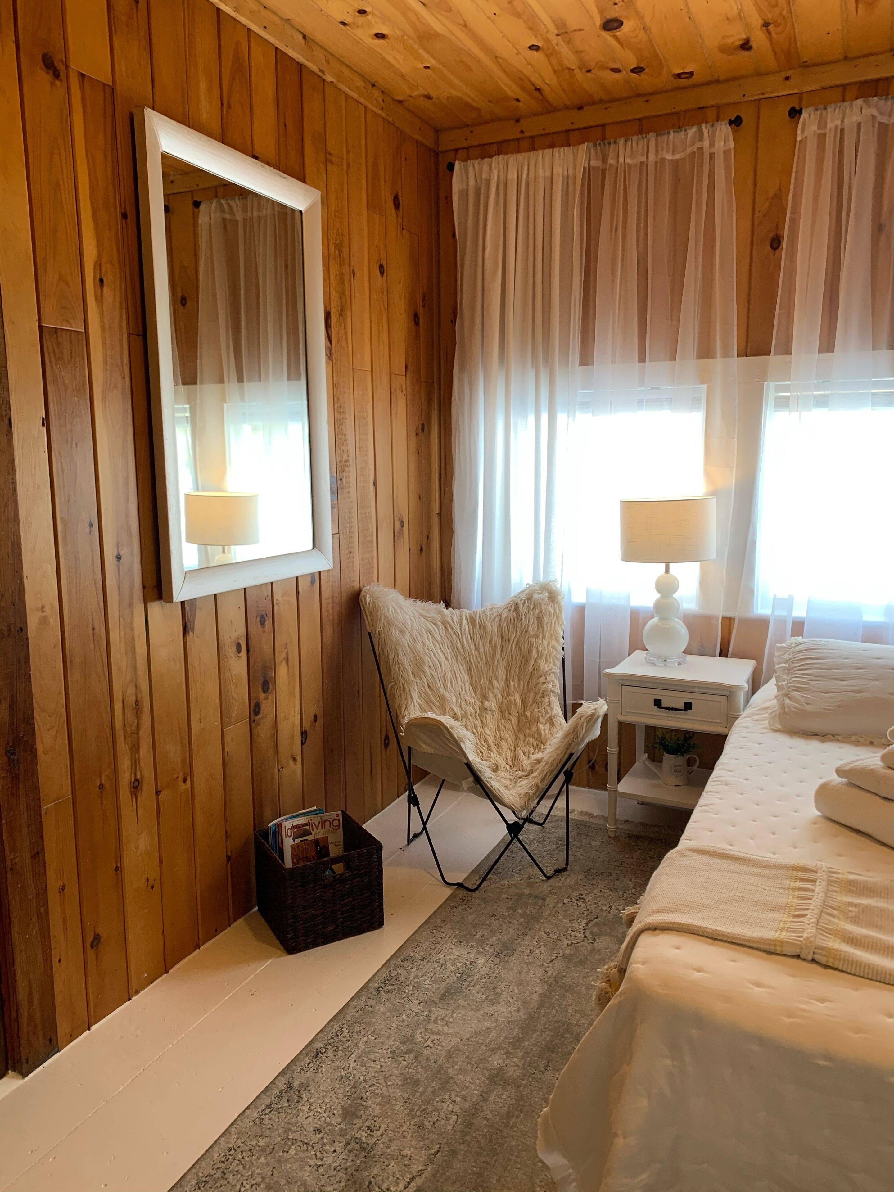 A wooden-paneled room with a bed, a chair, a nightstand, and a mirror.