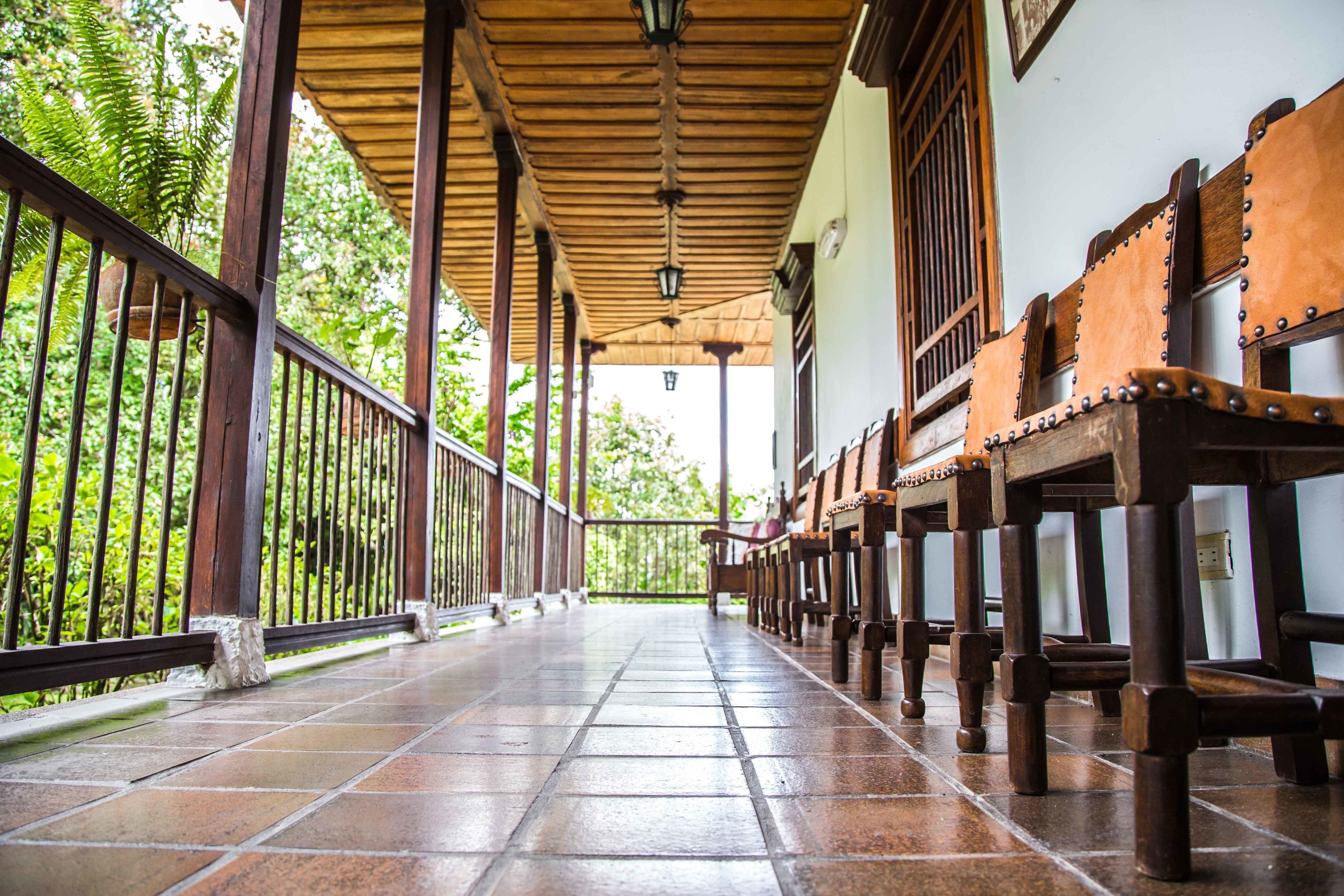 A covered corridor with wooden benches and a tiled floor, flanked by metal railings and greenery.