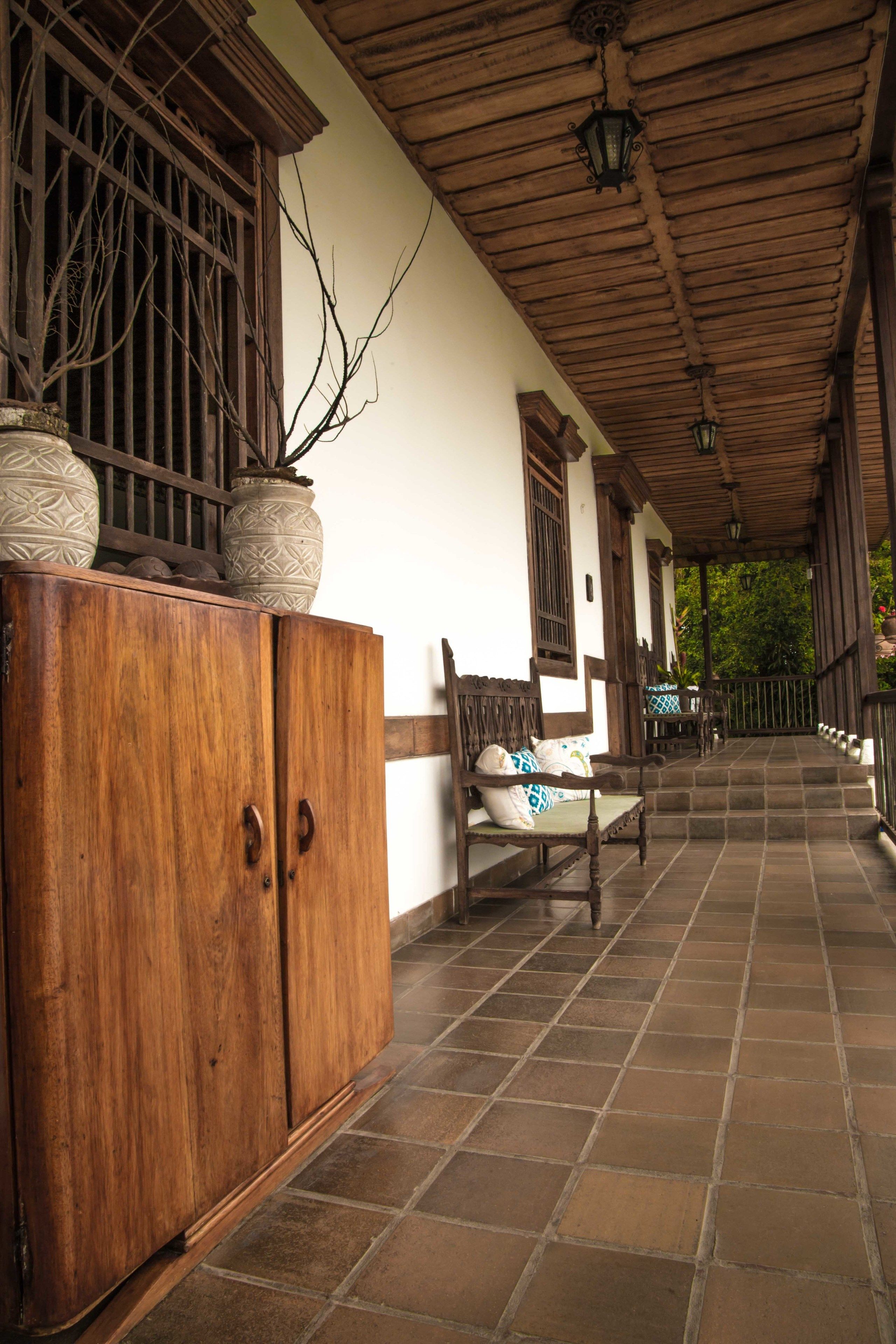 A covered outdoor area with a wooden bench, a cabinet, and a tiled floor.