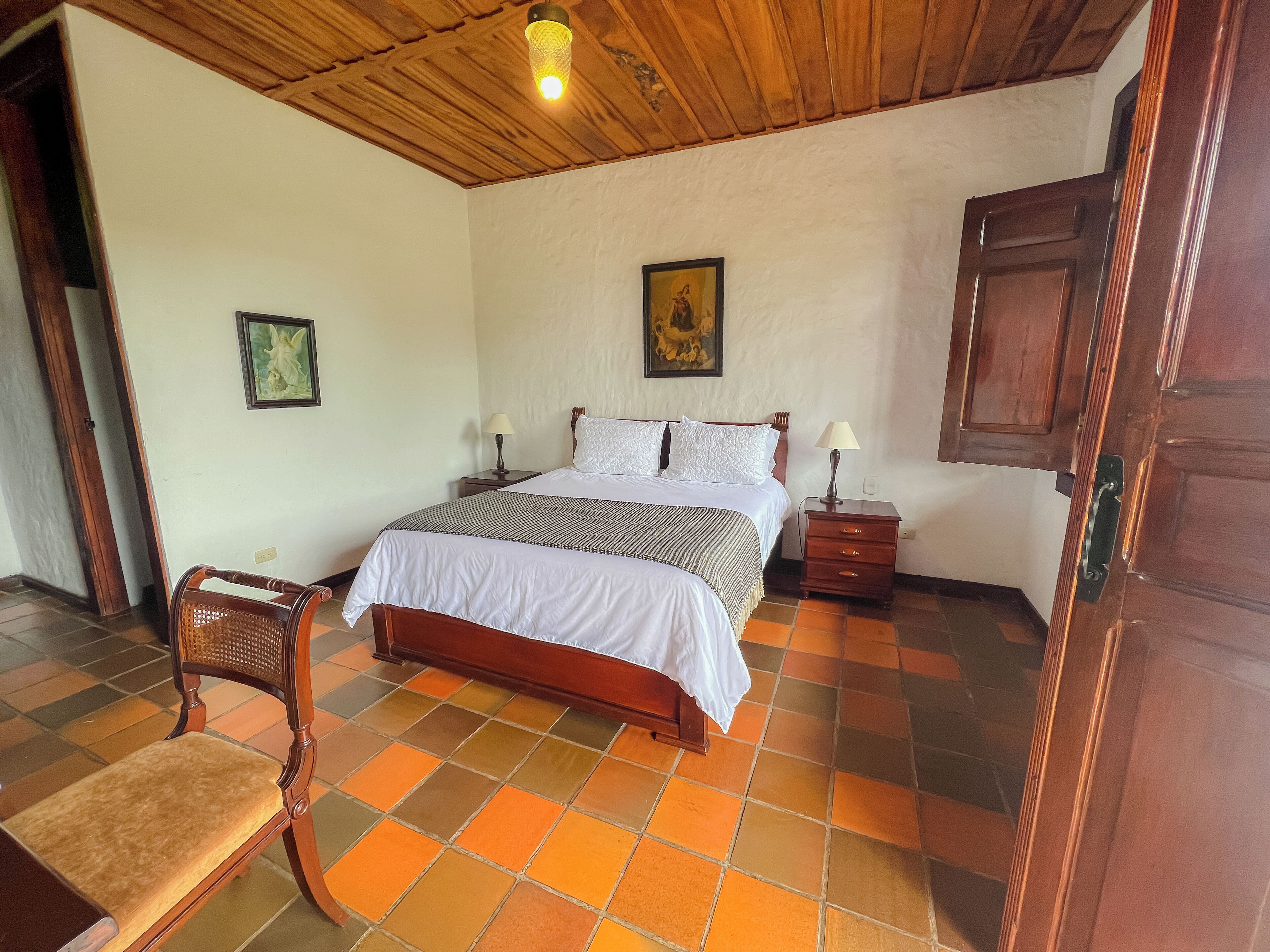 Un dormitorio con techo de madera, una cama con ropa de cama blanca, una mesita de noche, una silla y una puerta.