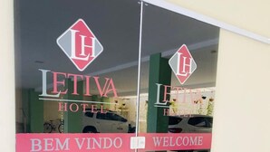 Entrada de un hotel con un felpudo rojo y una puerta de cristal que muestra el nombre del hotel y un mensaje de bienvenida.