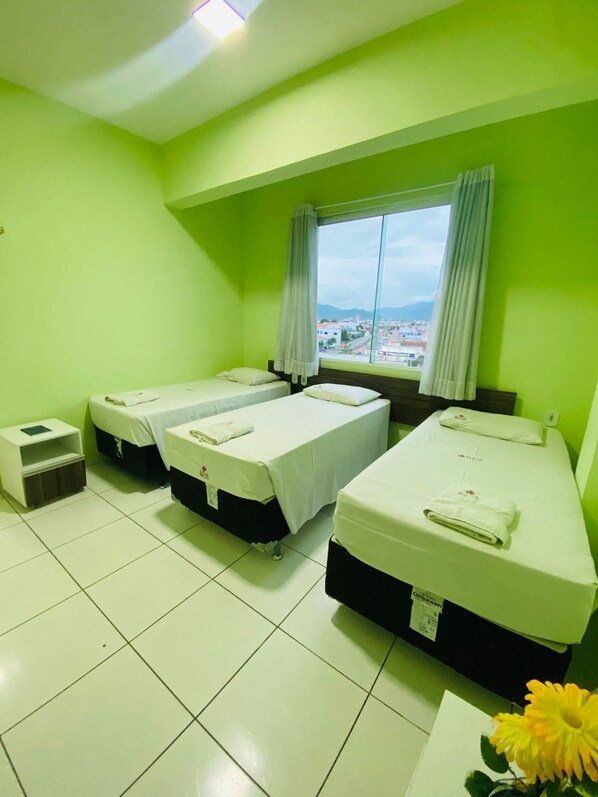 Habitación de hotel con tres camas individuales, una mesita y una ventana con vista a la ciudad.
