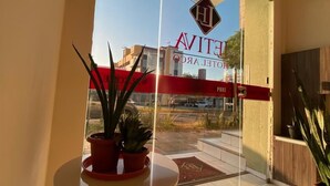 Entrada de un hotel con puerta de cristal, una mesita con plantas en macetas y vista a la calle.