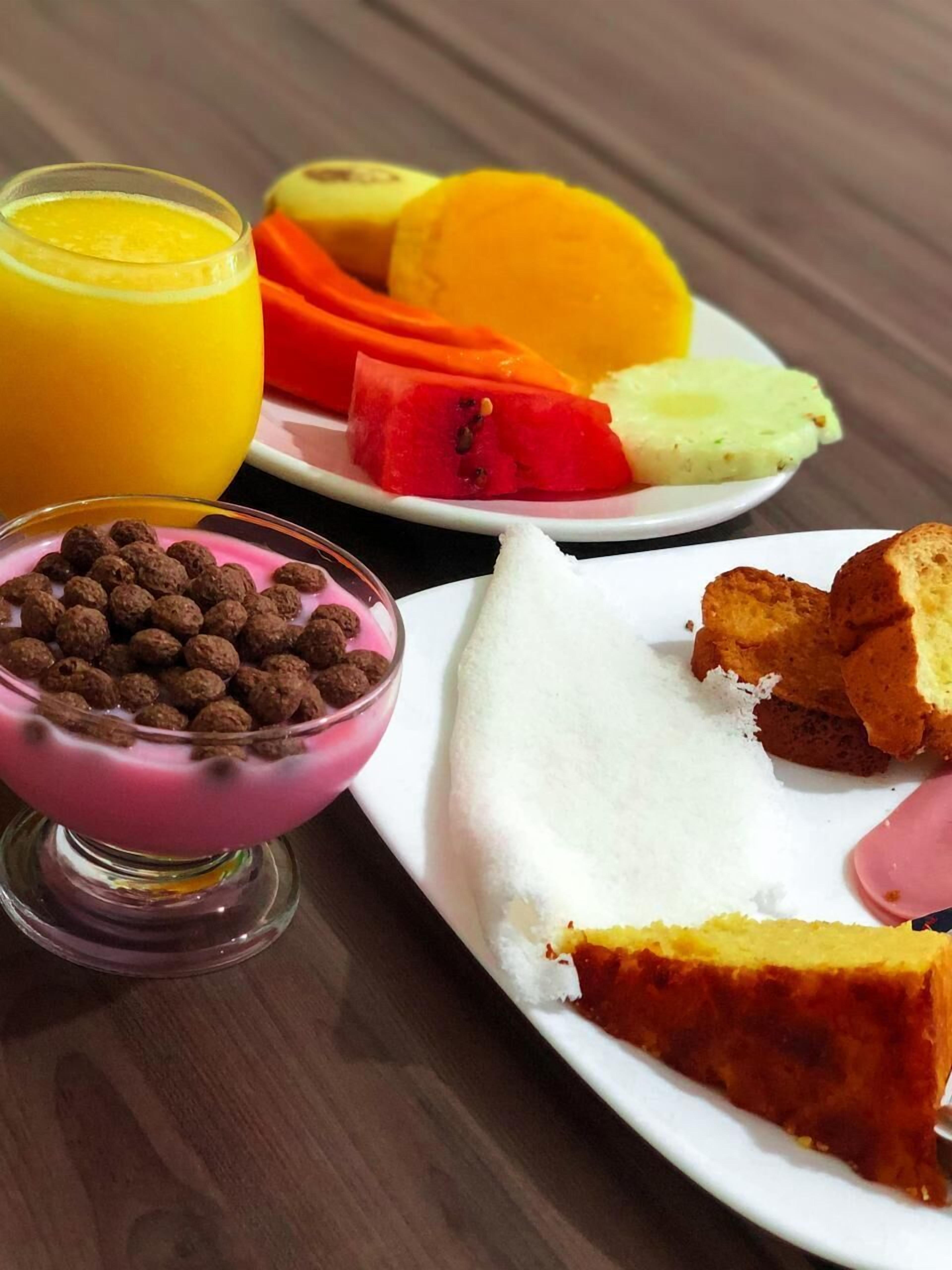 A breakfast plate with a slice of cake, a bowl of cereal, and a glass of orange juice.