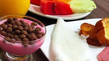 A breakfast plate with a slice of cake, a bowl of cereal, and a glass of orange juice.