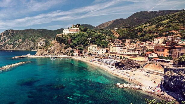A coastal town with a clear blue sea, a rocky coastline, and buildings on the hillside.