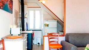 A compact living space with a kitchen area, a dining table with chairs, a sofa, and a staircase leading to an upper level.