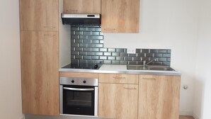 A compact kitchen with wooden cabinets, a black tiled backsplash, a stainless steel sink, and a built-in oven.