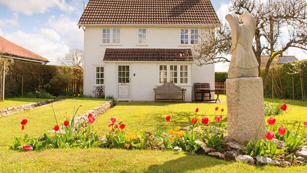 A white house with a brown tiled roof, a stone statue, and a garden with red tulips.