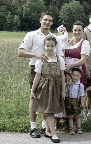 A family outdoors with a grassy field and trees in the background.