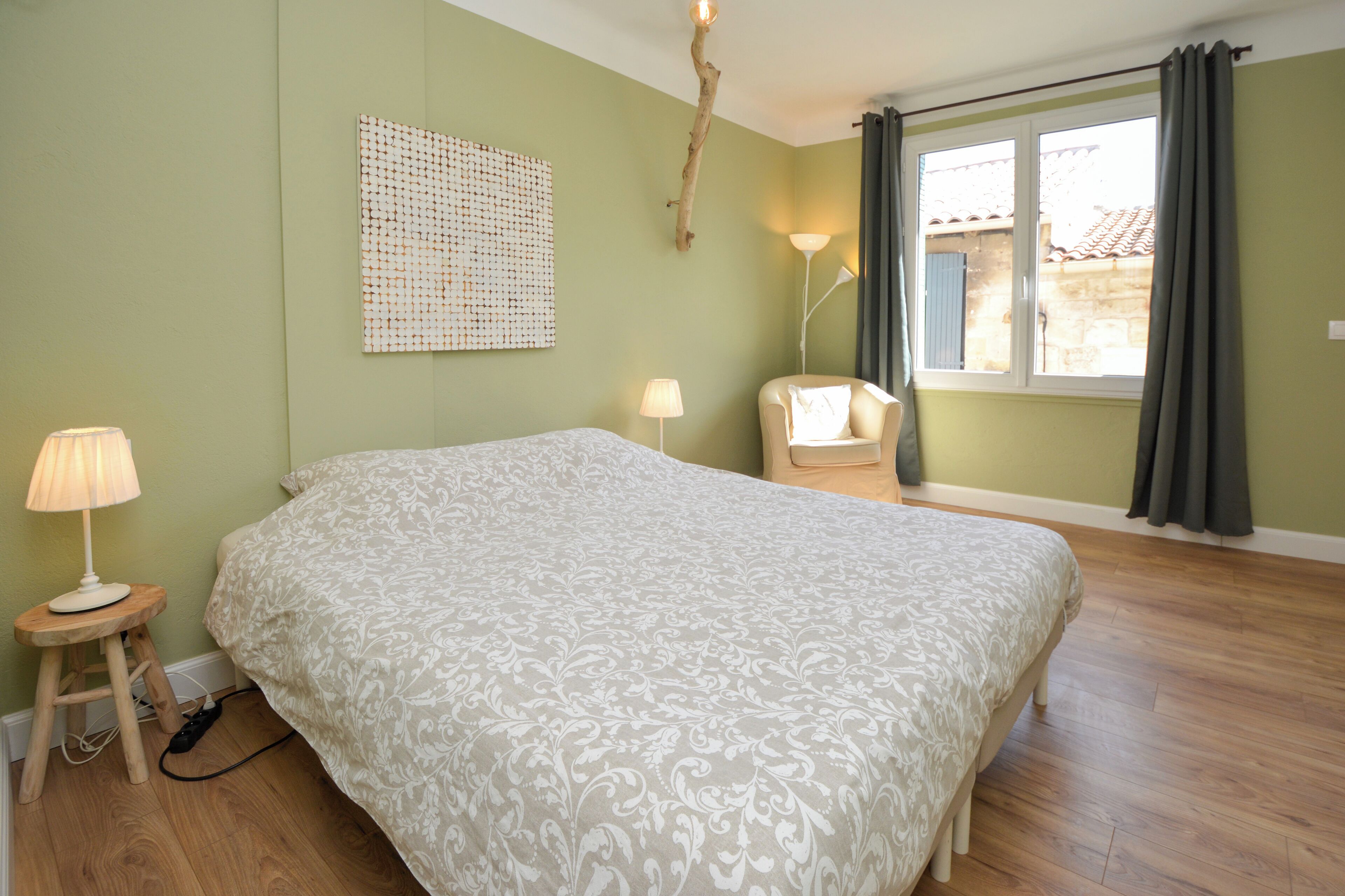 Un dormitorio con una cama grande, una silla, una lámpara y un ventanal con cortinas.