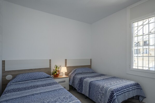 A bedroom with two beds, a nightstand, a lamp, and a window with a view of buildings. - Amazing apartment on the seafront in Roses Inmosantos Oasis F5 (Rosas / Roses)