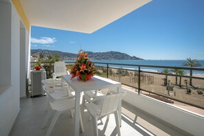 A balcony with a white table and chairs, a flower vase, and a view of the beach and mountains. - Amazing apartment on the seafront in Roses Inmosantos Oasis F5 (Rosas / Roses)