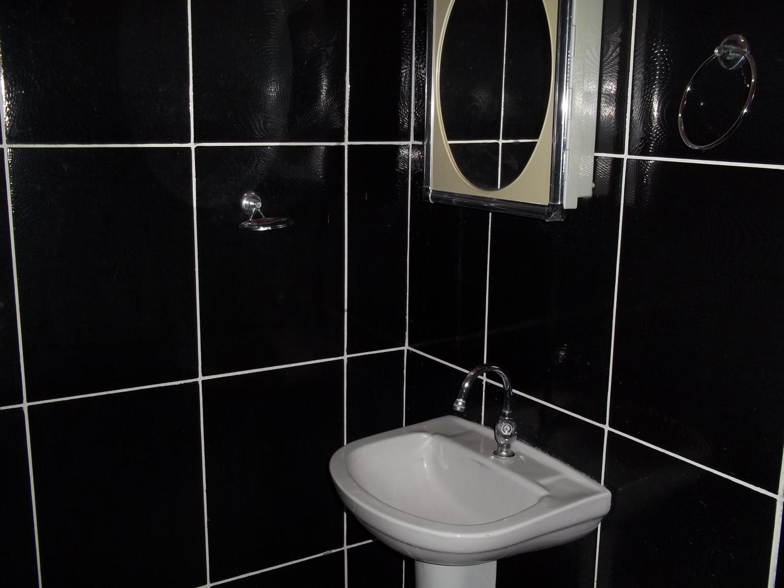 Casa de banho com lavatório branco, espelho e paredes revestidas a mosaico preto.