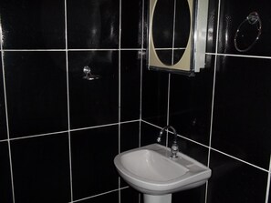 A bathroom with a white sink, a mirror, and black tiled walls.
