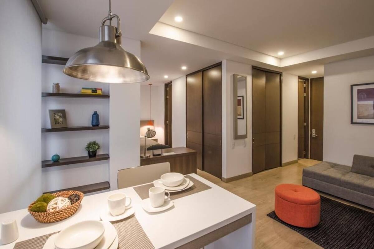 Un salon moderne avec un coin repas, comprenant une table mise avec des assiettes et des tasses, un canapé et un pouf rouge.