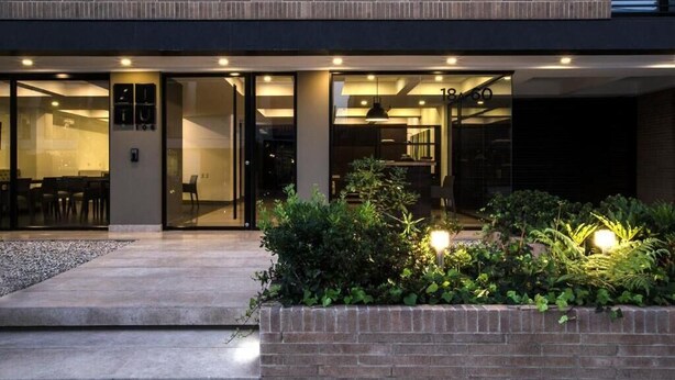 A modern building with a glass entrance, a well-lit outdoor area with plants, and a visible number "18/60" on the facade. - ZITU 106 (Bogotá)