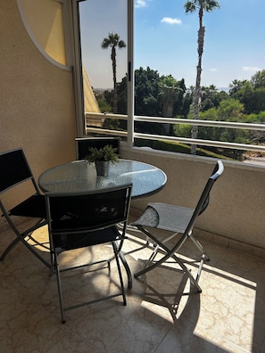 Enjoy a peaceful retreat on this balcony overlooking lush greenery and palm trees.