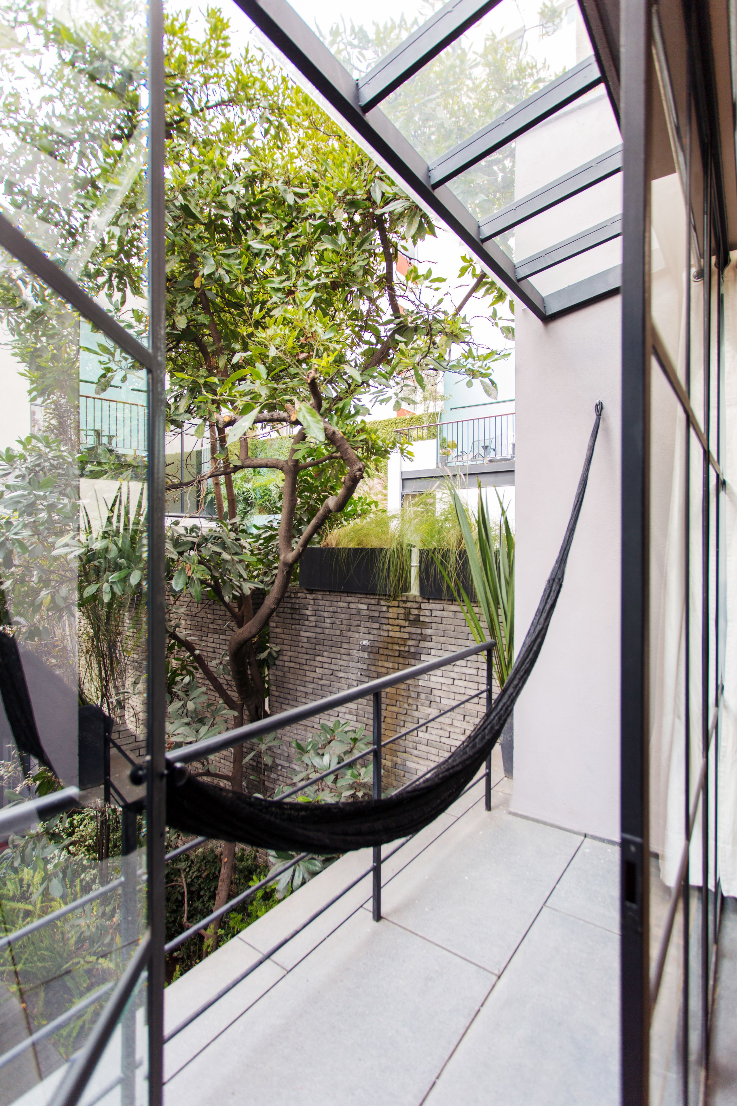 Un interior moderno con barandilla de cristal que da a un patio con un árbol y plantas.