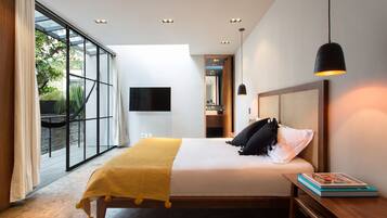 A modern bedroom with a large bed, a bedside table, a TV mounted on the wall, and a view of the outdoors through a glass door.