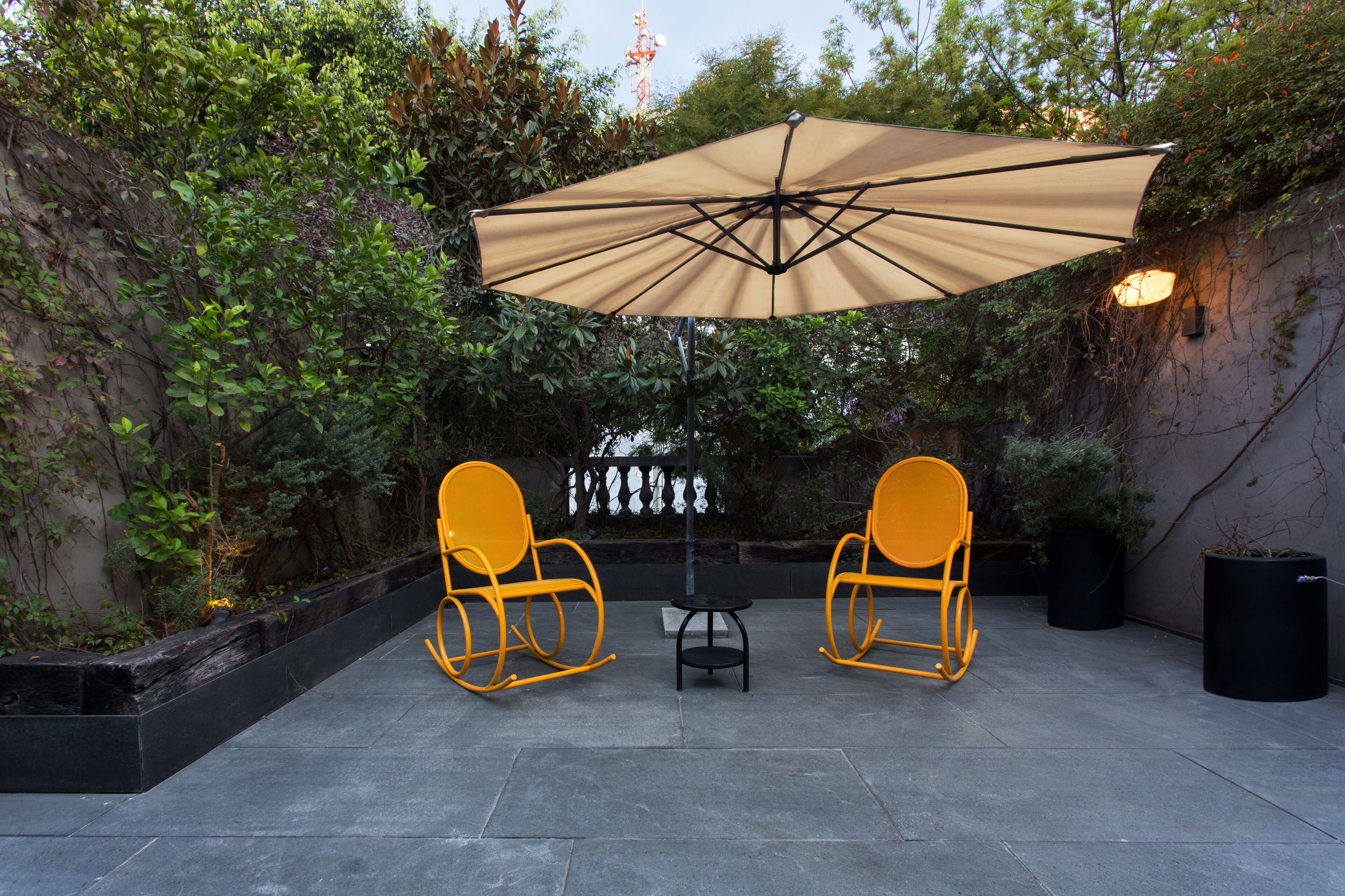 An outdoor patio with two yellow rocking chairs, a table, and a large beige umbrella.