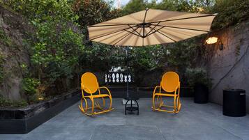 An outdoor patio with two yellow rocking chairs, a table, and a large beige umbrella.