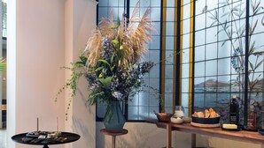 A corner room with a large window, a wooden table with a vase of flowers, and a black table with cutlery. - Casa 9 (Mexico City)