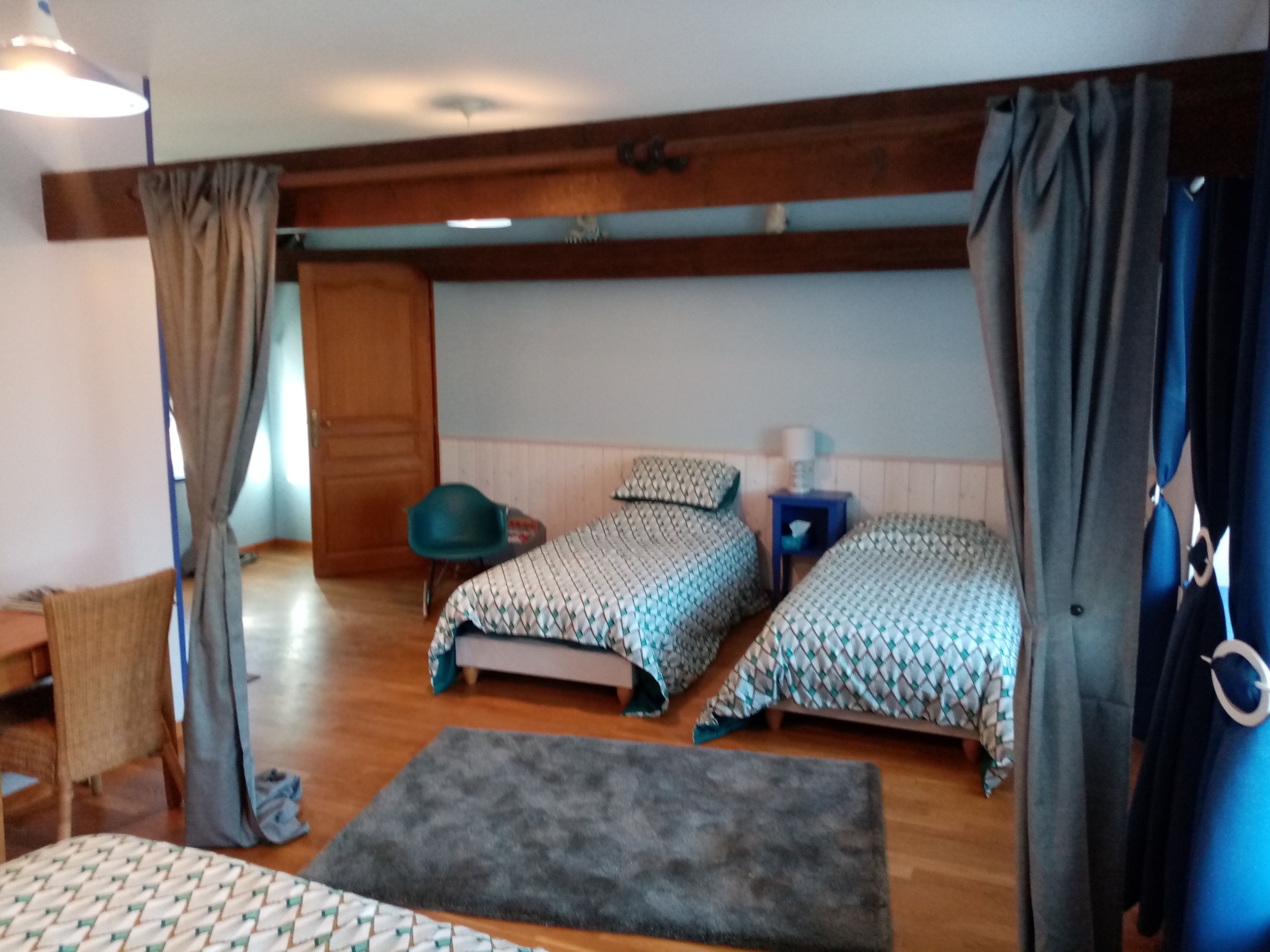 Een kamer met twee bedden, een stoel, een tafeltje en een raam met gordijnen.