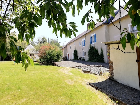 A residential property with a well-maintained lawn, a stone pathway, and a house with a tiled roof and blue shutters.