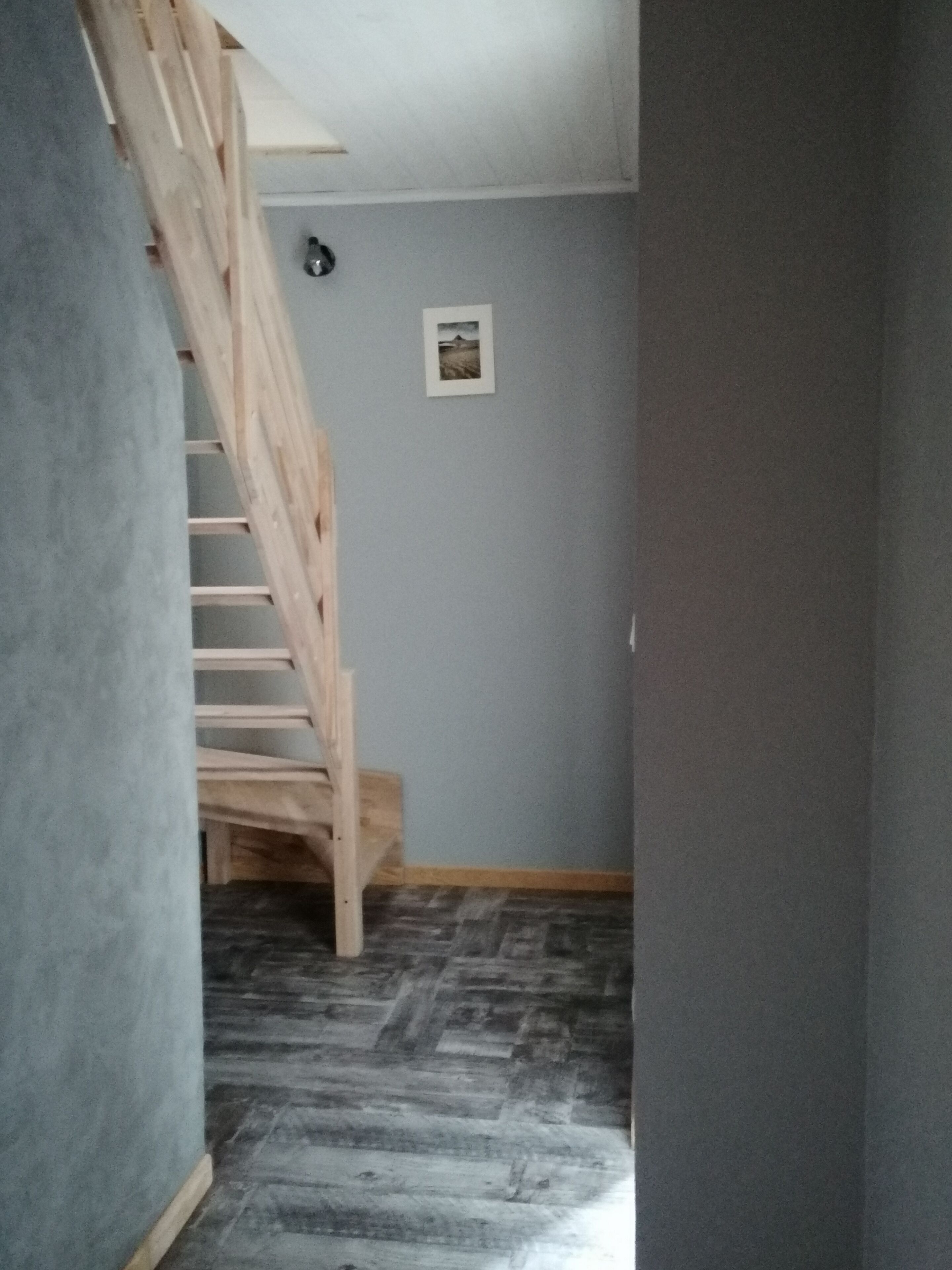 Una escalera de madera conduce a un rellano, con un pequeño cuadro en la pared y un suelo con diseño.