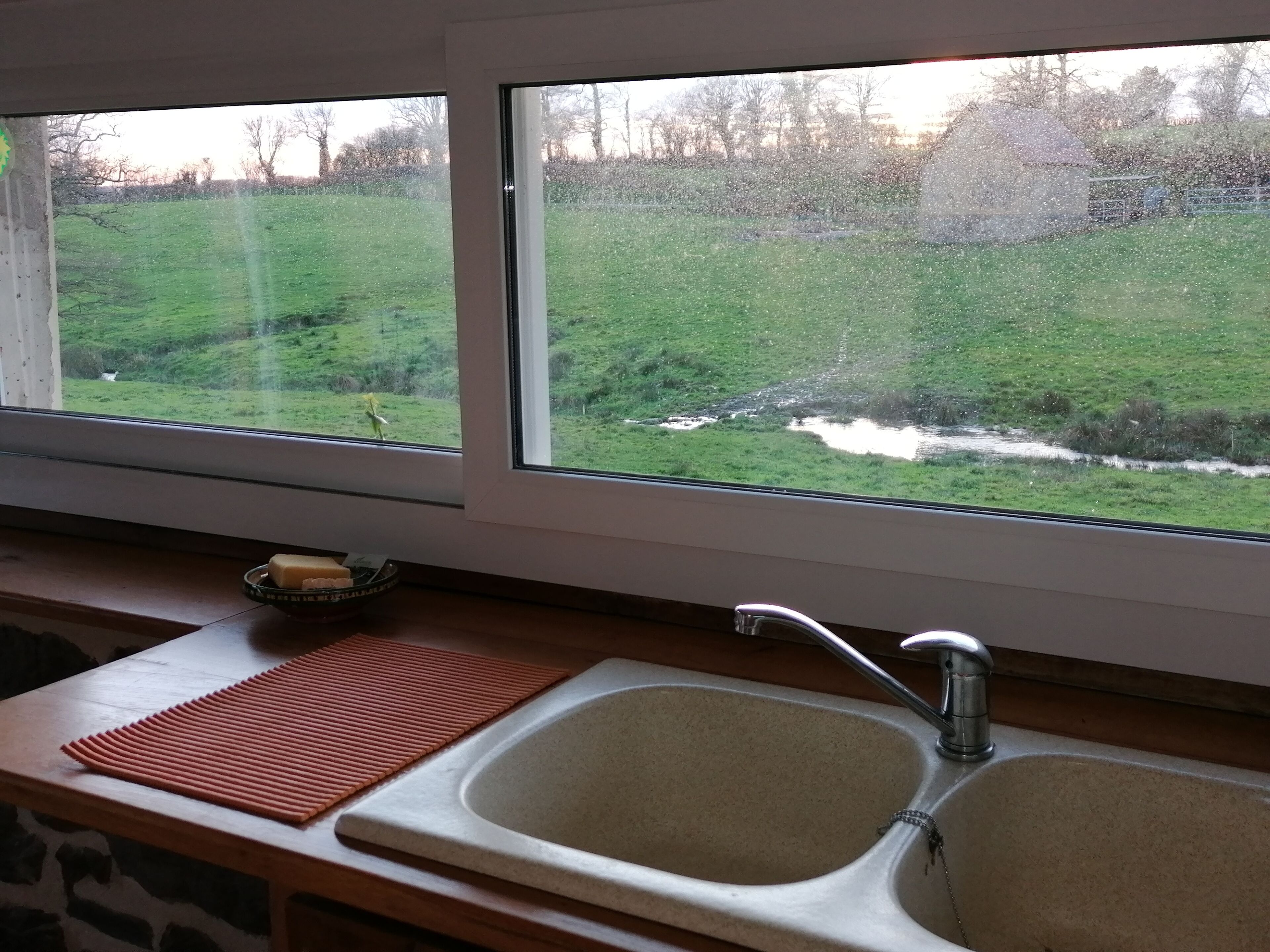 Cozinha com pia dupla e janela com vista para uma área gramada.