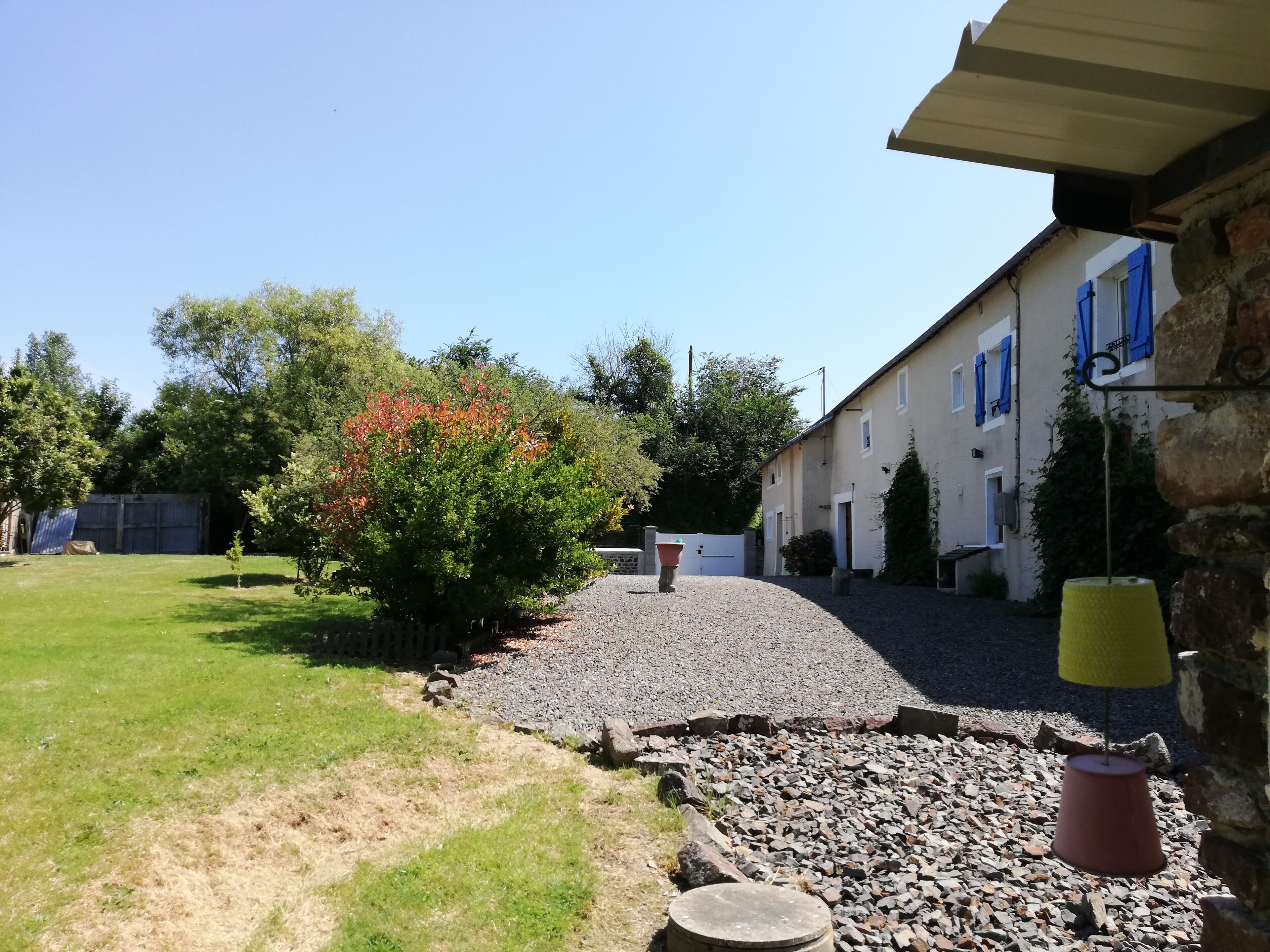 A courtyard with a gravel path, a small tree with red leaves, and a building with blue shutters.