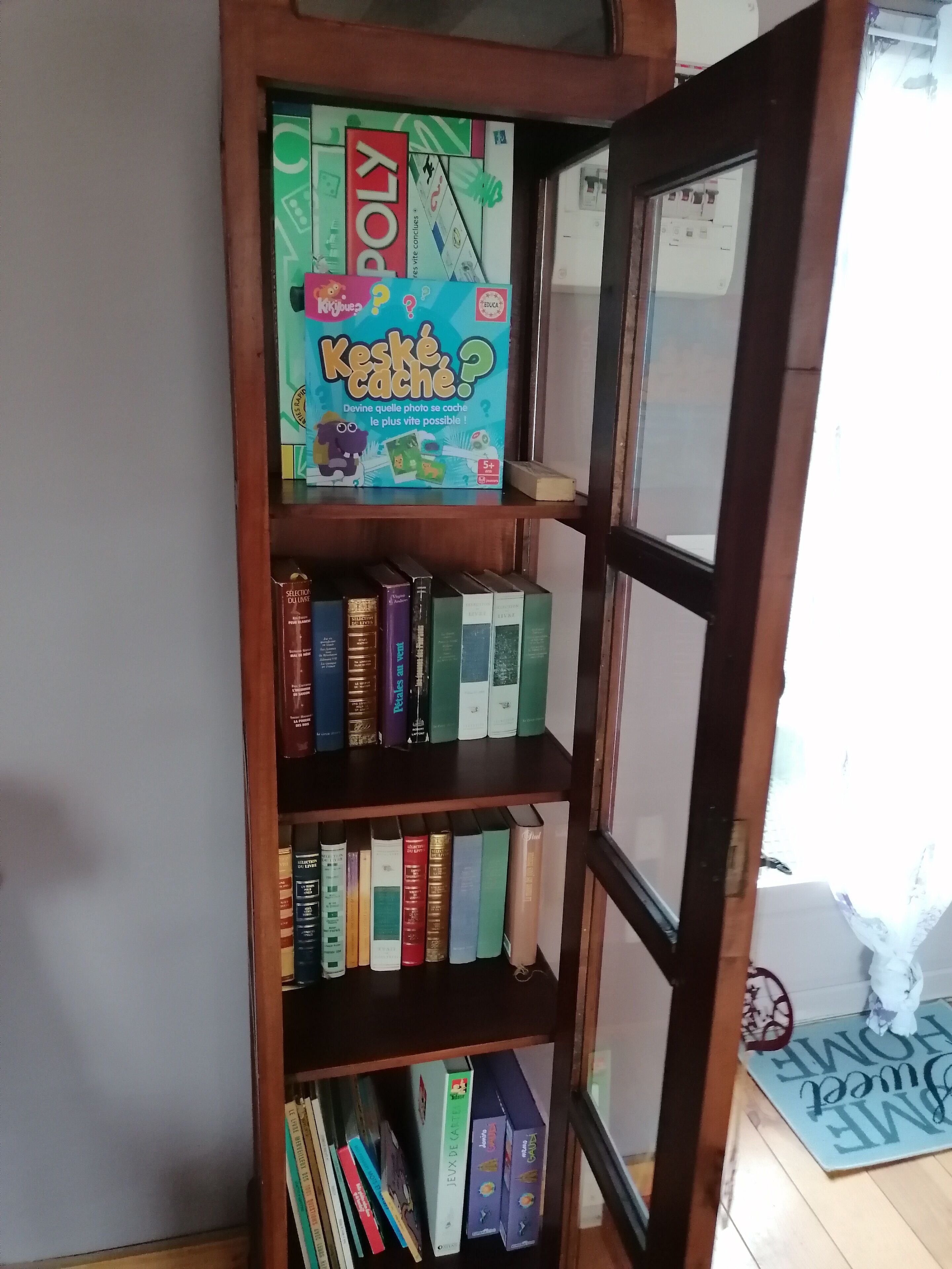 A bookshelf with various books and a board game titled 'Keské Cache?'