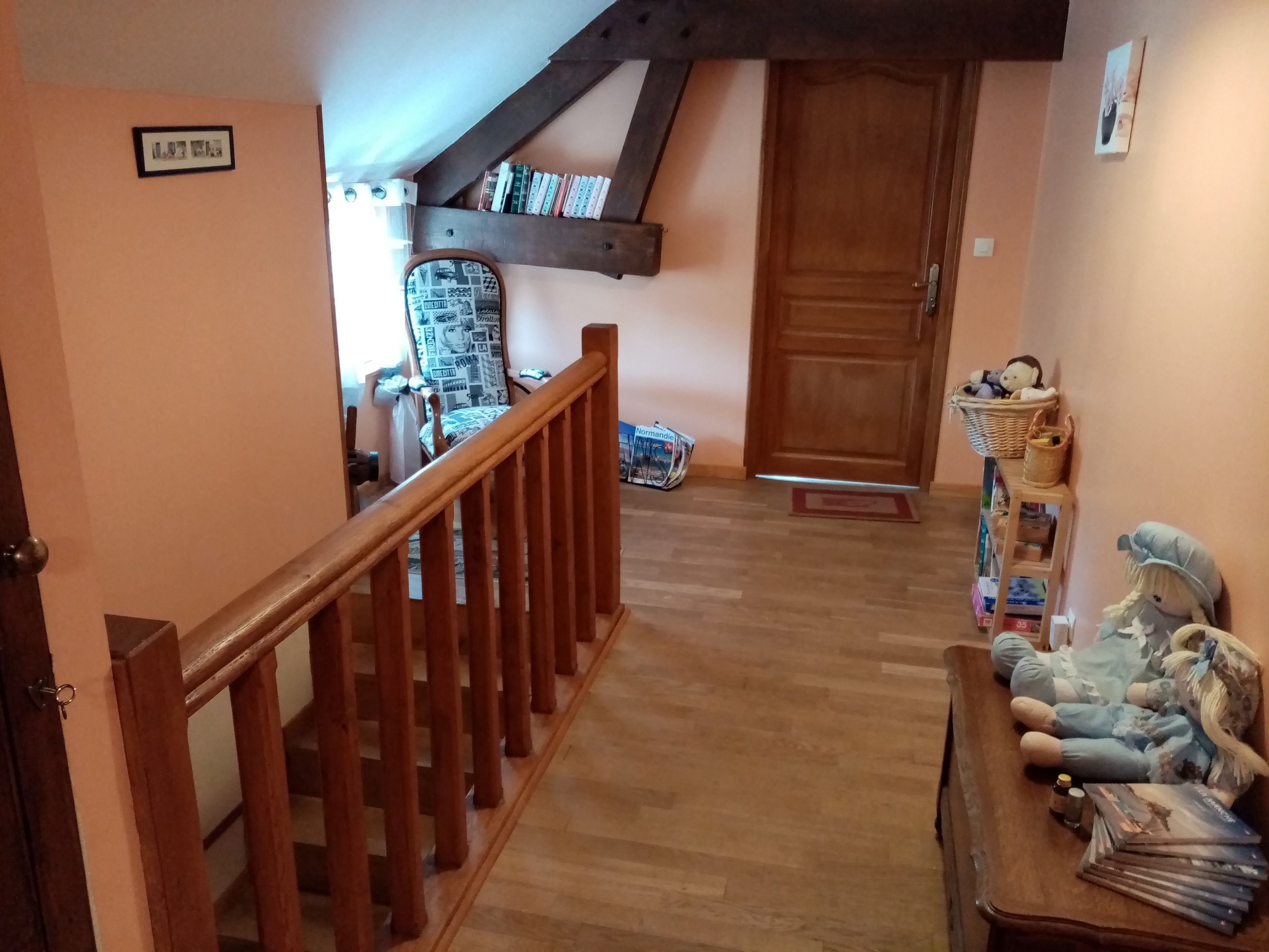 Una escalera de madera conduce a una plataforma con una estantería, un sillón con estampado y una puerta.