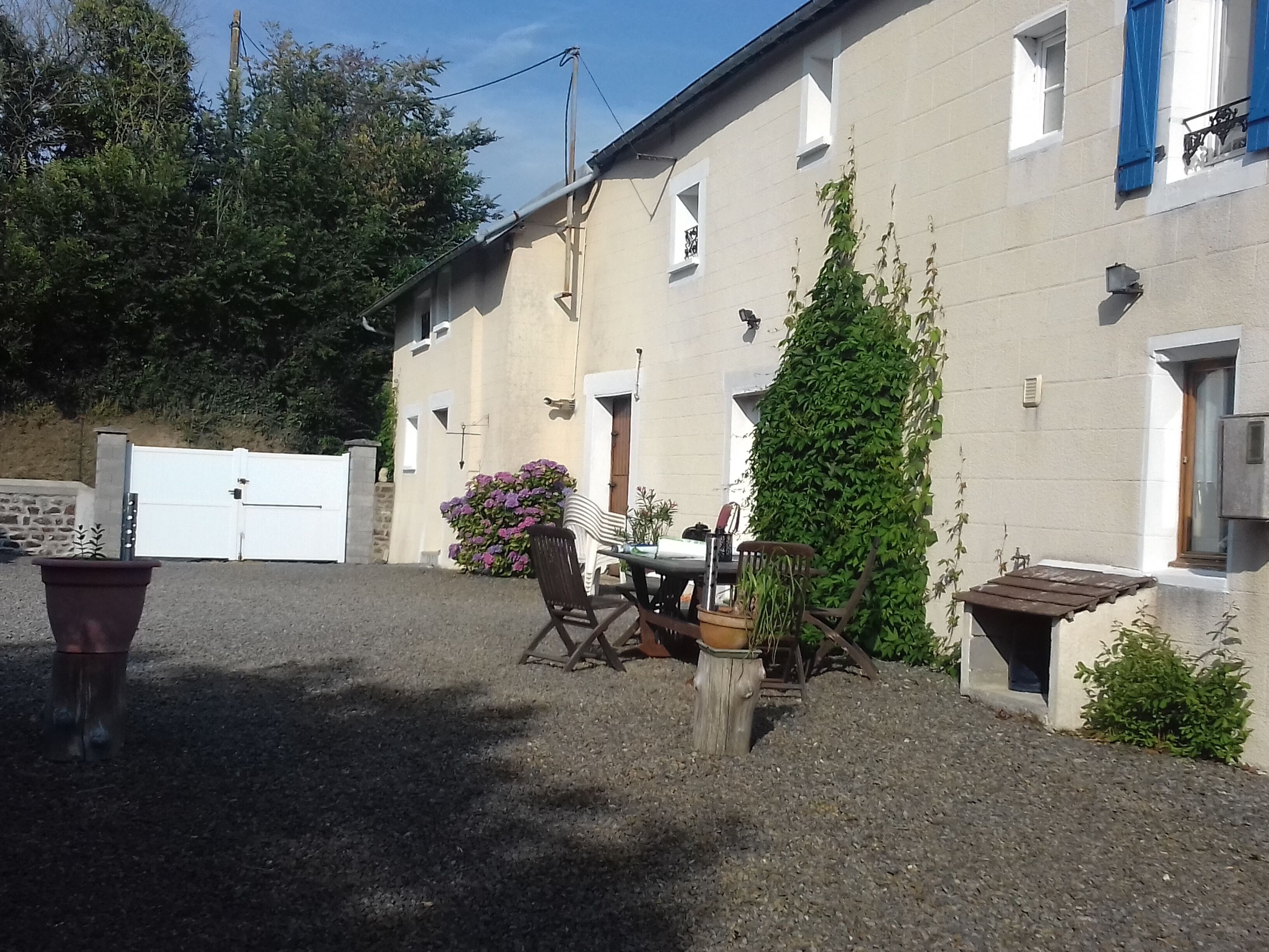 A building with a gravel driveway, a wooden table with chairs, and a potted plant.