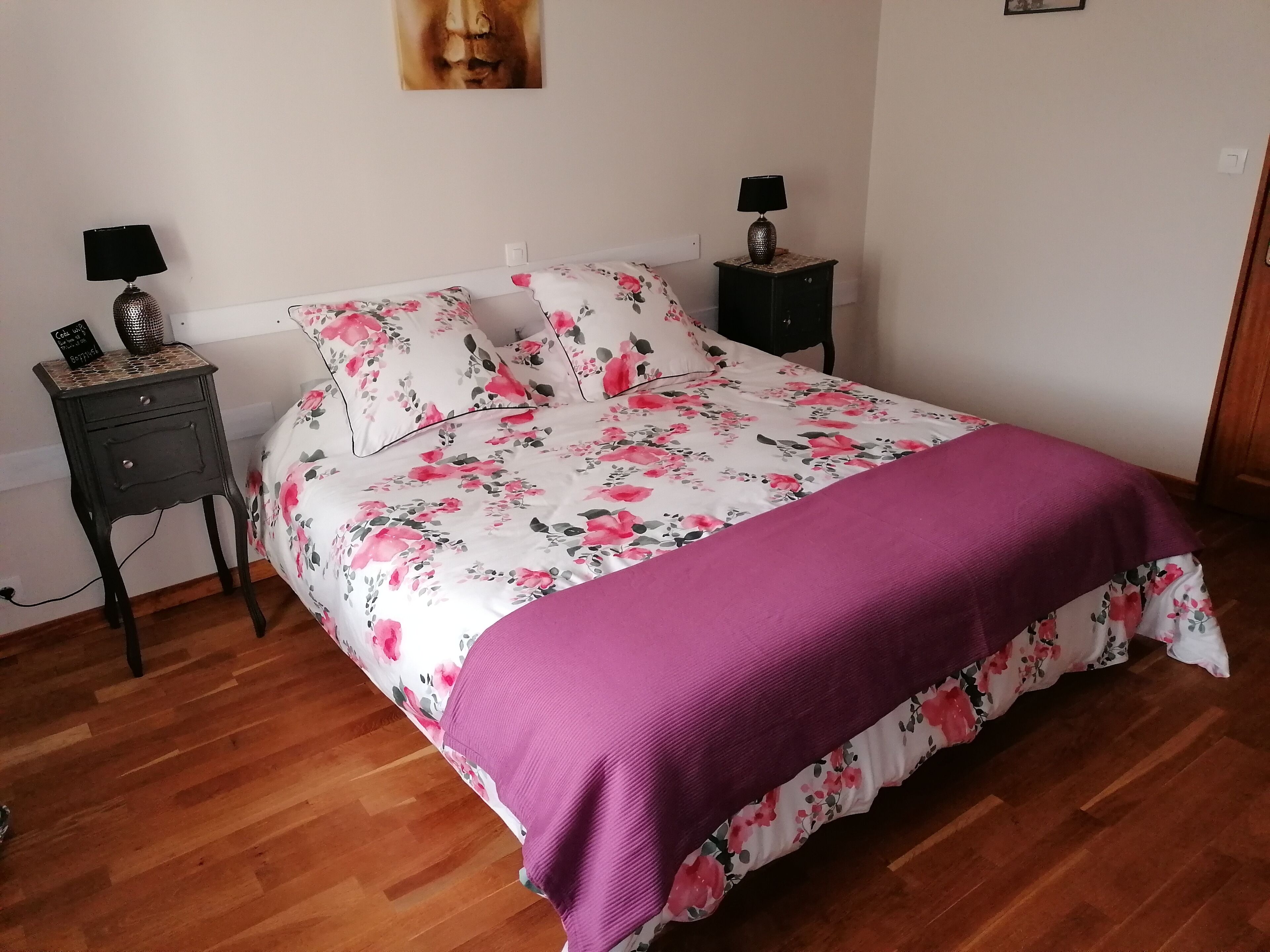 A bedroom with a floral bedspread, a purple throw blanket, and two bedside tables with lamps.