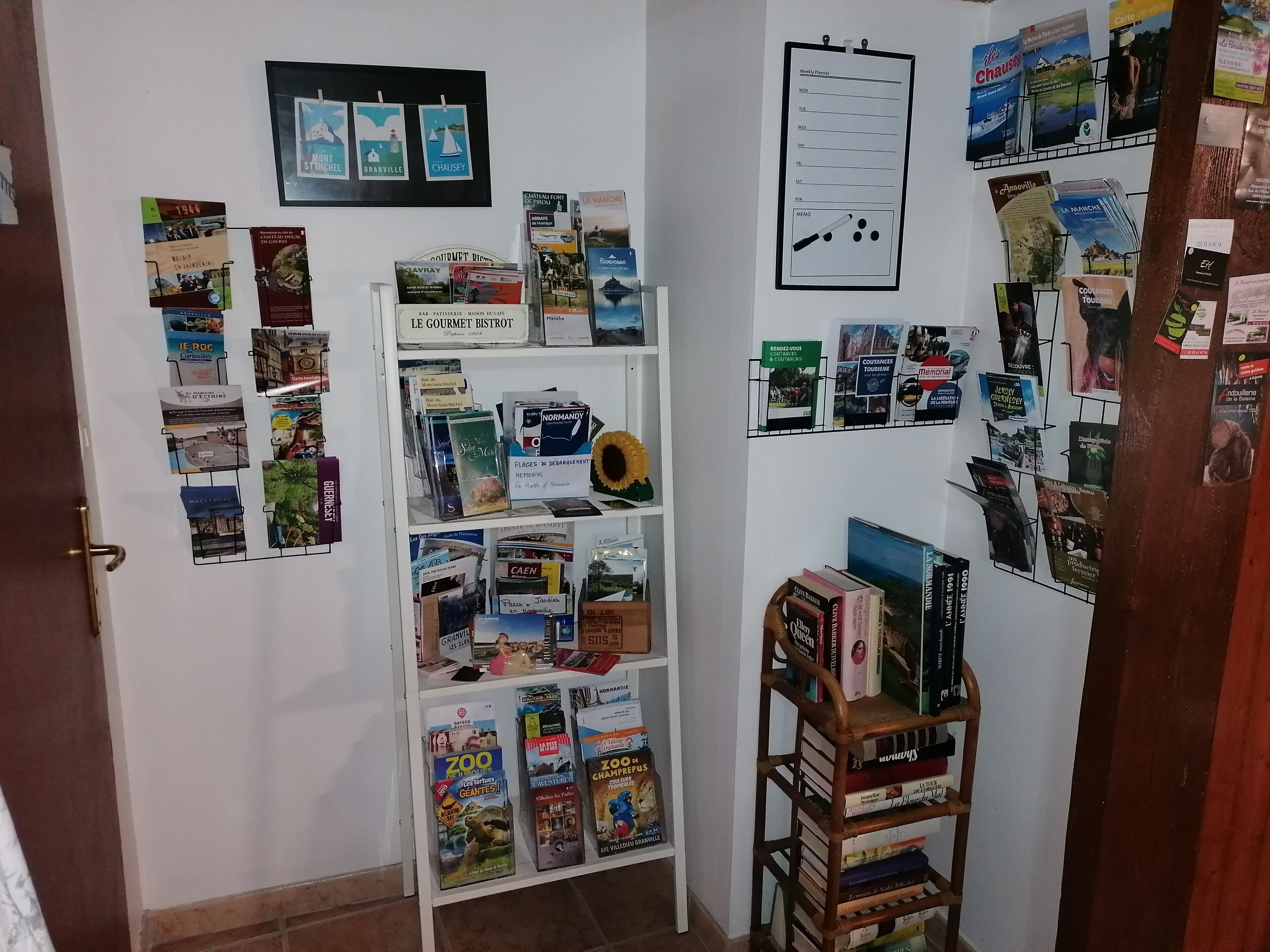 Una habitación con una pared blanca que incluye un calendario, una pizarra y varios folletos de viajes.