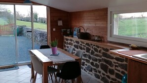 Un coin repas comprenant une table, des chaises, une plante en pot, un mur en pierre et une fenêtre donnant sur un jardin.