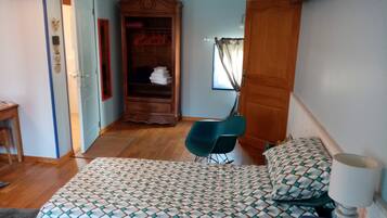 Un dormitorio con una colcha estampada, un armario de madera, una silla azul y una mesita de noche con lámpara.