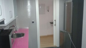 Cocina compacta con pileta, refrigerador y una puerta que da a un pasillo.