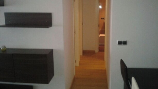 Un pasillo con un armario de madera oscura a la izquierda, una pared de tonos claros y una puerta al final que da a otra habitación.