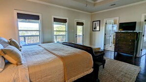 A bedroom with a large bed, a dresser, a television, and a balcony view.