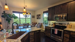 A kitchen with dark wooden cabinets, a granite countertop, a built-in oven, and a large window providing natural light.