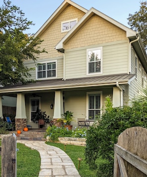 Une maison à deux étages avec un porche couvert, des marches en pierre et une clôture en bois.